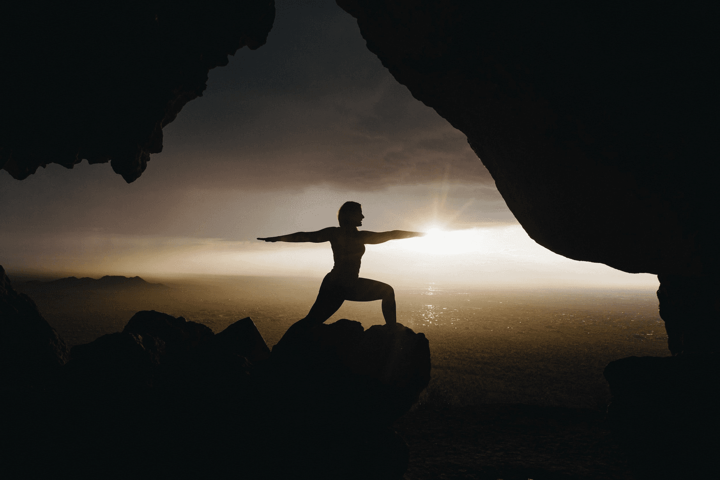 Silhouette of a person doing yoga in a cave at sunset