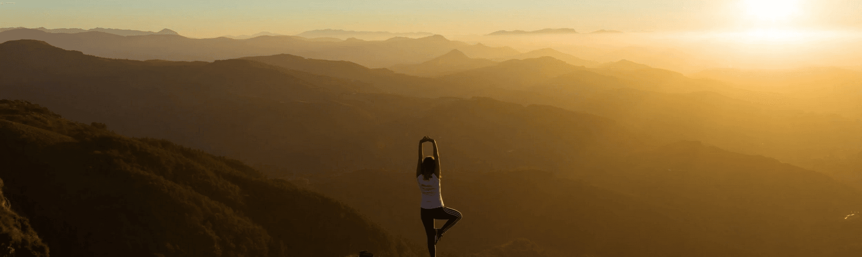 Woman doing yoga on a mountain at sunset